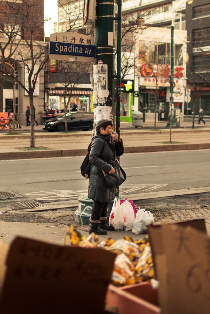 A woman standing with plastic bags full of items on the ground next to her.