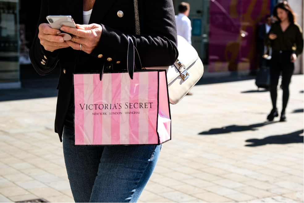 A woman carrying a paper bag printed with Victoria's Secret.